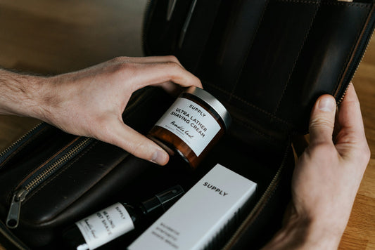 Hands packing a small amber glass jar into a black toiletry bag
